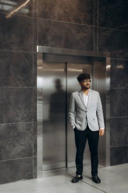 İyi giyimli bir birey asansörün yanında duruyor, profesyonellik ve modern mimari tasarım sergiliyor..