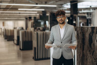 Çağdaş bir ofiste iyi giyimli bir profesyonel elinde belgeler, güven ve liderliği temsil ediyor. Kuruluşta modern iç tasarım, yaratıcılık ve verimlilik sergileniyor..