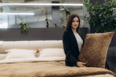 Modern dekor ve doğal yeşillik içeren lüks bir yastığı modern bir yatak odasında tutan profesyonel giyinmiş bir kadın. Konforlu, misafirperver ve şık bir ortam düzenleme ve düzenleme ile iletilir..