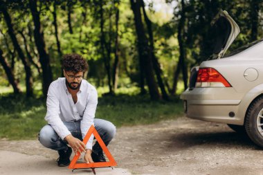 Adam yol kenarına kırmızı bir güvenlik üçgeni yerleştiriyor, bir araba arızası sinyali veriyor ve yardıma ihtiyacı var. Erişim araçları için bagajı aç