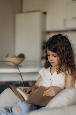 Evde rahat bir şekilde otururken kitap okumaya dalmış genç bir kız. Oda çalışma ve rahatlık için ideal sakin ve sıcak bir atmosfere sahip..