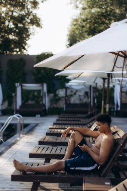 Yaz tatilinin tadını çıkaran bir turist, güneş altında güneşlenirken akıllı telefonunu kullanıyor.