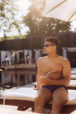 Turist havuz kenarında dinlenirken ferahlatıcı bir kokteylin tadını çıkarıyor, dinlendirici bir yaz tatili sırasında güneşi emiyor.