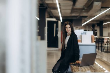 Profesyonel bir kadın şık bir ofis ortamında dizüstü bilgisayarla şık duruyor. Kurumsal, mesleki ve ofis ile ilgili kavramlar için ideal betimleme, güveni yansıtan, işyeri dinamiği ve kariyer ilerlemesi.