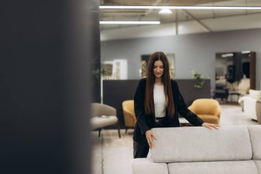 İyi giyimli bir kadın zarif ve çağdaş bir mobilya galerisinde açık renkli bir kanepeyi inceler, çeşitli dekorlar ve çağdaş tasarımlar sergiler..