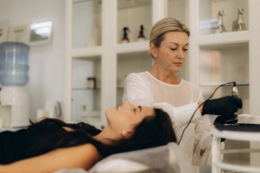 Bir güzellik salonunda müşterinin kaşlarına kalıcı makyaj yapan dövme sanatçısı kozmetik geliştirmeyi sembolize ediyor.