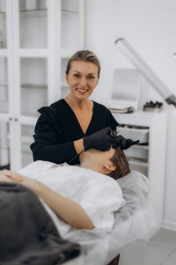 Modern bir güzellik salonunda müşterinin kaşlarına kalıcı makyaj uygulayan profesyonel bir güzellik uzmanı.