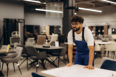 Tulumlu genç adam perakende satış mağazasında modern mobilyalar düzenliyor müşteriler ve satışlar için yer hazırlıyor.