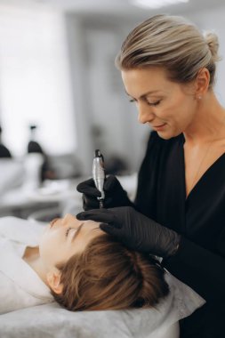 Kadın güzellik uzmanı müşteriye kalıcı makyaj kaşları çiziyor. Mükemmel kaşlar için güzellik salonu tedavisine odaklan.