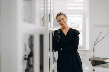 Siyah üniformalı profesyonel kozmetik uzmanı gülümsüyor, elinde mikromakyaj kalemi tutuyor, modern bir güzellik salonunda ya da klinikte çalışıyor.