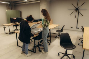 Çağdaş bir ofis ortamında birlikte çalışan iki meslektaş, bir belge tarama görevine odaklanıyor. Çalışma alanı minimalist dekor ve geniş masa alanı içeriyor, üretkenliği ve takım çalışmasını teşvik ediyor.