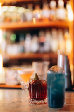 Bir bar tezgahında canlı renklerle sergilenen el yapımı kokteyller, odaklanmış arka plan ışıklandırmasıyla birlikte, sosyal toplantılar ve içecek keyfi için sıcak ve davetkar bir atmosfer yaratıyor..