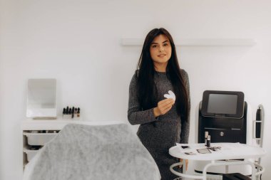 Elinde kozmetik göz bantları tutan bir kadın, modern bir güzellik salonunda ya da klinikte duruyor, kirpik kaldırma işlemine hazır.