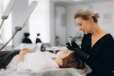 Güzellik uzmanı bir güzellik salonunda genç bir kadının kaşlarına kozmetik mikroplar sürüyor, yüz hatlarını geliştiriyor.