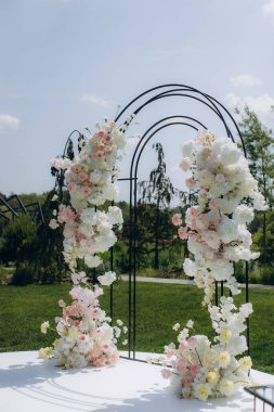 Beyaz ve pembe çiçek aranjmanlarının yer aldığı zarif bir düğün kemeri, bahçede romantik bir seremoni düzenliyor.
