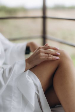 Beyaz cüppeli bir kadın, zarif bir yüzük ve yumuşak bir manikürle rahatlamış, sakin bir sabahın tadını çıkarıyor, şımartıyor ve narin cilt bakımını yapıyor.