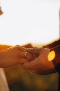 Kadın ve erkek el ele tutuşuyor, evlilik ve nişan yüzüklerini sergiliyorlar, aşkı, bağlılığı ve evliliği simgeliyorlar.