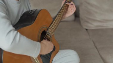 Kadın evde akustik gitar çalıyor. Akustik gitar çalan kadın eller. Yakın çekim..