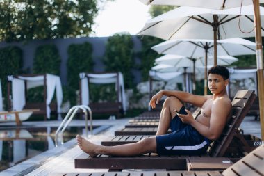 Gençler yaz tatilinin tadını çıkarıyor, güneşli bir günde akıllı telefonuyla havuz kenarında dinleniyor.