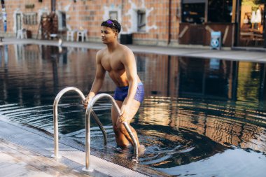 Genç erkek yüzücü yoğun bir eğitim seansını tamamladıktan sonra merdiven kullanarak havuzdan çıkıyor.