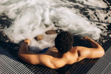 Genç adam, şampanyalı bir jakuzide rahatlamanın tadını çıkarıyor. Huzurlu bir spa merkezinde huzurlu bir günün tadını çıkarıyor.