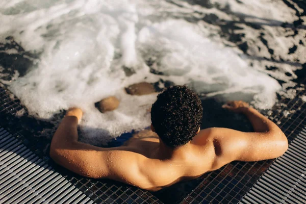 Genç adam, şampanyalı bir jakuzide rahatlamanın tadını çıkarıyor. Huzurlu bir spa merkezinde huzurlu bir günün tadını çıkarıyor.