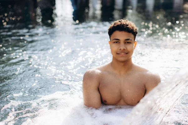 Genç adam sıcak, kaynayan suyla çevrili, sıcak bir banyoda rahatlatıcı bir spa gününün tadını çıkarıyor ve nihai rahatlığı kucaklıyor.