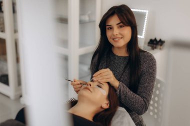 Profesyonel bir güzellik uzmanı müşterinin gözlerine takma kirpik takıyor kuaför salonunda güzellik prosedürü uyguluyor.