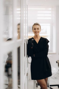 Profesyonel kadın kozmetik uzmanı elinde kalıcı bir makyaj makinesi tutuyor, gülümsüyor ve modern bir güzellik salonunda duruyor.