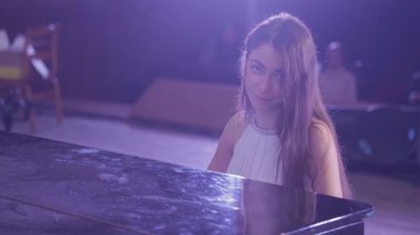 Beyaz Elbiseli Genç Kadın Mor Işıklar Altında Sahnede Tutkuyla Piyano Çalıyor. Güzel ve Duygusal Müzikal Performans.