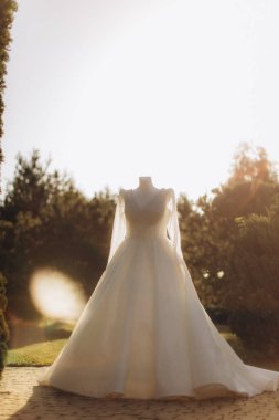 Uzun kollu beyaz bir gelinlik ve kafasız bir mankenin üzerinde detaylı bir korse. Dışarıda güneşli bir bahçede duruyor.