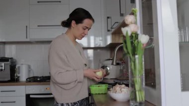 Ev hanımı, mutfak tezgahında beyaz soğan soyarken dikkatli bir şekilde ev yemeği için taze malzemeler hazırlıyor.