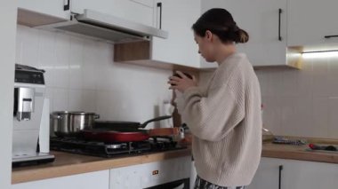 Kadın modern mutfak sobasında ev yapımı yemek hazırlıyor, günlük ev işleri sırasında parlak ve temiz mutfak alanında taze malzemeler pişiriyor.