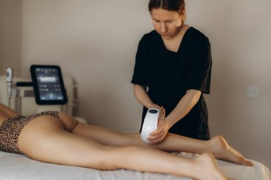 Modern bir tıbbi kaplıcada kadın bacağı üzerinde profesyonelce bitiş terapisi uyguluyor. Anti-selülit ve deri sıkılaştırma üzerine yoğunlaşıyor.