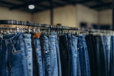 Bir perakende mağazasında askıda asılı duran mavi kot pantolonlar müşteriler için çeşitli stil ve boylar sunuyor.