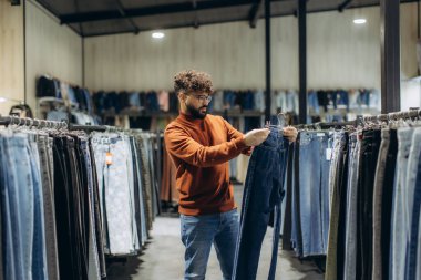Modern bir giyim mağazasından yeni kot pantolon seçen bir adam, mükemmel uyumu ve tarzı arıyor.
