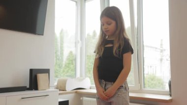 Genç bir kız dans hareketlerini oturma odasında yapıyor. Rutinini mükemmelleştirirken kollarını uzatır ve gülümser..