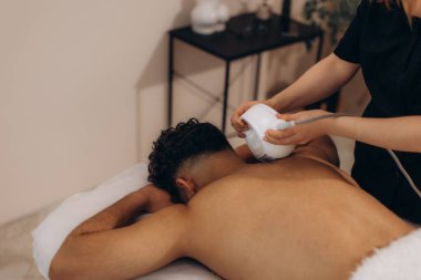 Adam spa yatağında dinleniyor, profesyonel bir terapistten özel bir aletle sırt masajı yaptırıyor. Vücut ve sırt için endosphere masaj