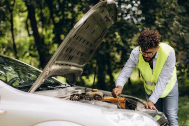 Yüksek görüş mesafesi olan bir adam yol kenarındaki bir araba arızasından sonra motor yağını dipstick ile kontrol ediyor.