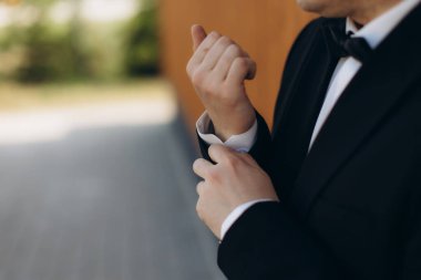 Siyah smokinli adam kutlamaya hazırlanıyor. Damat elleri dikkatlice kol düğmesini ayarlıyor, tören için hazır.