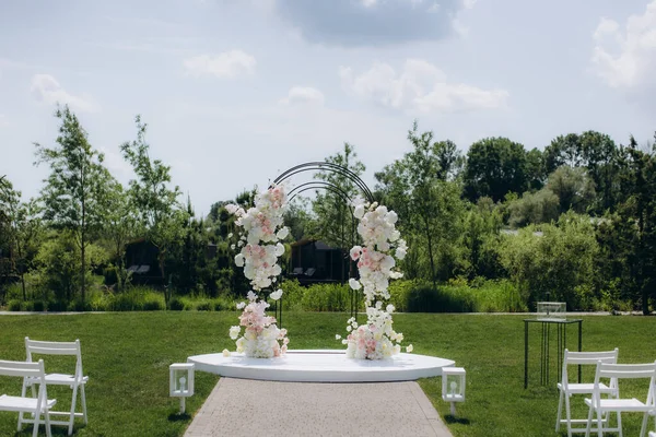 Beyaz sahnede pembe ve beyaz çiçekli zarif düğün kemeri, açık hava seremonisi için hazırlanıyor.