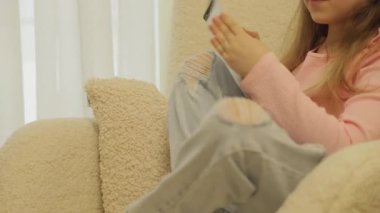 Genç bir kız bej bir koltukta rahatça oturup defterine çizim yapıyor. Pembe gömlek ve yırtık kot pantolon giyiyor..