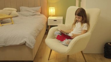 Evde Tablet Bilgisayar kullanan genç kız. Yatak odasında rahat koltuğa oturur, interneti gezer ya da oyunlar oynar..