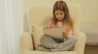 Genç bir kız rahat bir şekilde bir sandalyede oturup defterine çizim yapıyor. Uzaklara bakarken hayal gücü bir gülücük saçıyor..