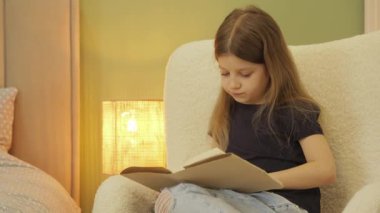 Genç Kız Evde Samimi Bir Sandalyede Kitap Okuyor. Sıcak ışık huzurlu bir atmosfer yaratır..
