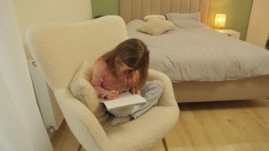 Koltuğunda oturan ve albümünü çizen küçük kız. Çocuk, Yaratıcı Faaliyetine yoğunlaşır.