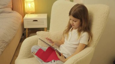 Evde Tablet Kullanan Genç Kız. Çocuk oyunları oynuyor. Kol Sandalyesinde Dinlenen Çocuk Dijital Cihaz Kullanıyor. Modern Teknoloji Konsepti.