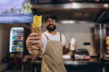 Önlüklü arkadaş canlısı şef fast food mutfağında lezzetli bir shawarma dürümü ve bir şişe süt ya da yoğurt ikram ediyor.