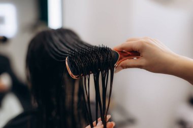Profesyonel bir el, saç fırçasıyla kadının ıslak siyah saçlarını tarıyor. Kuaförde saç kurutmadan önce saç ve saç şekillerini değiştiriyor.