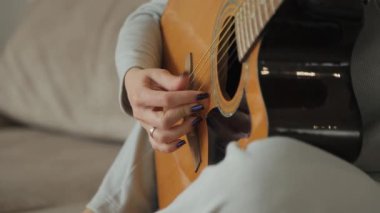 Kadın evde akustik gitar çalıyor. Kadın ellerinin gitar çalarkenki yakın çekimi. Sıcak ev atmosferi.